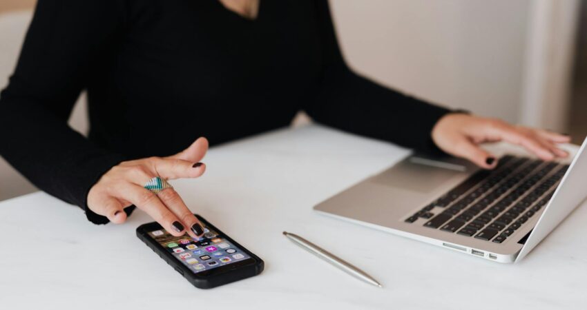 crop woman using smartphone and laptop during work in office