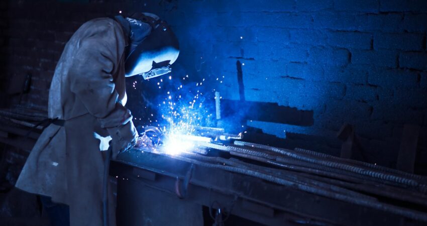 man wearing welding helmet welding metal near gray brick wall