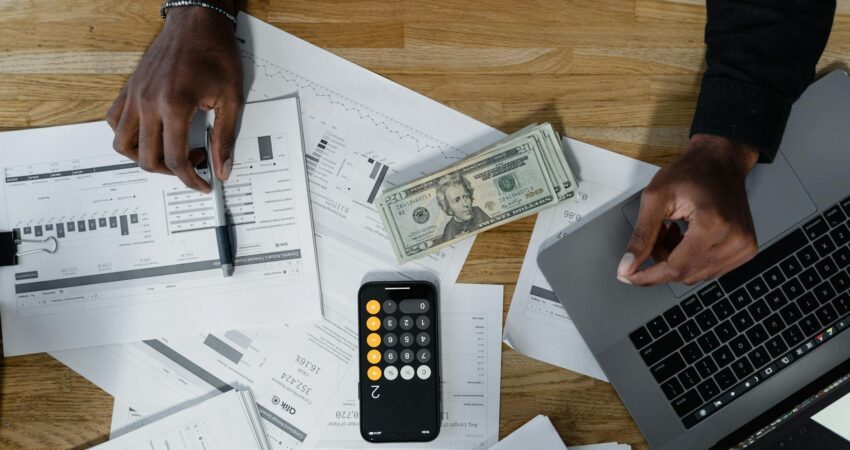 cash computer laptop pen and paperwork on wooden surface