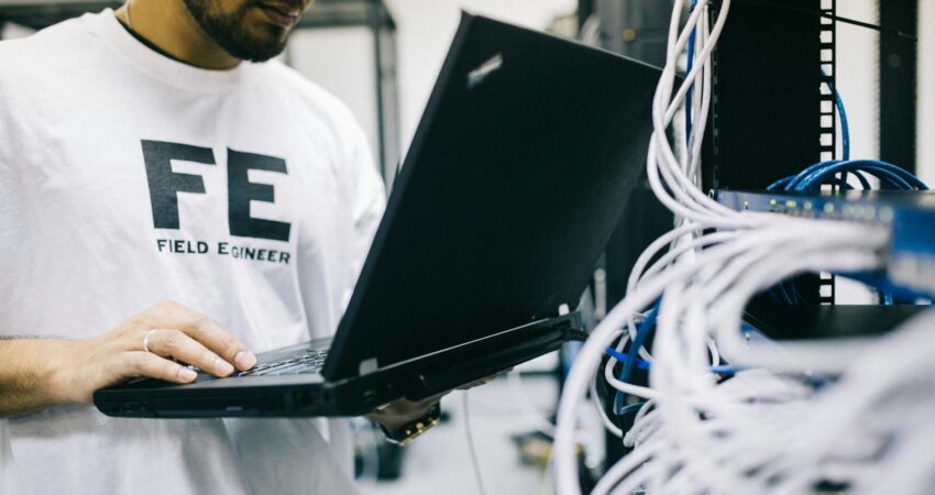 serious ethnic field engineer examining hardware and working on laptop