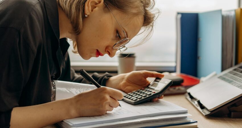 a woman writing on a book while holding a calculator