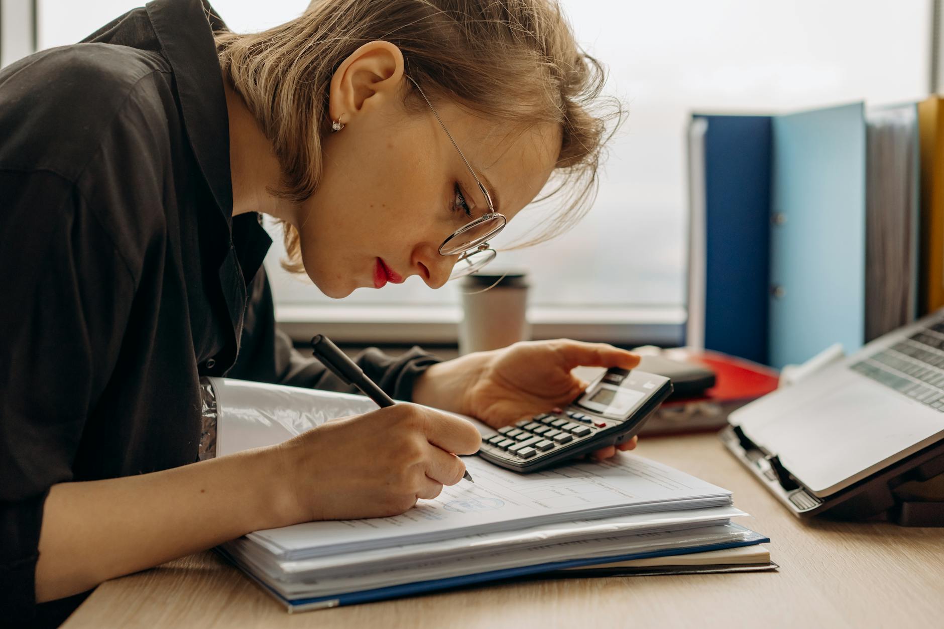 a woman writing on a book while holding a calculator