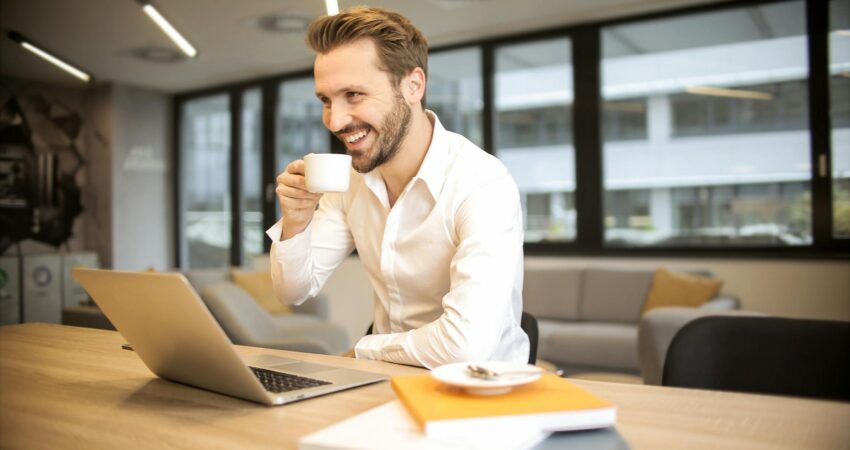 depth of field photo of man sitting on chair while holding cup in front of table